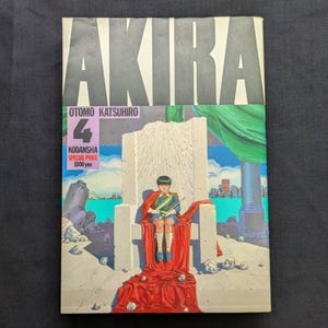 Könnte beinhalten: Akira Band 4 Manga-Buch. Das Cover zeigt eine junge Person in Militäruniform auf einem Thron sitzend. Der Titel "AKIRA" steht oben, darunter der Name des Autors und die Verlagsinformationen.