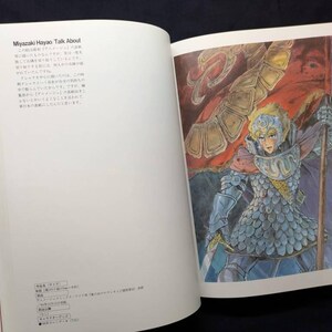 Pu&ograve; includere: Libro aperto con un'illustrazione colorata di un guerriero che tiene una bandiera. Il guerriero indossa un'armatura e un elmo. Il testo sulla pagina di sinistra recita "Miyazaki Hayao Talk About".
