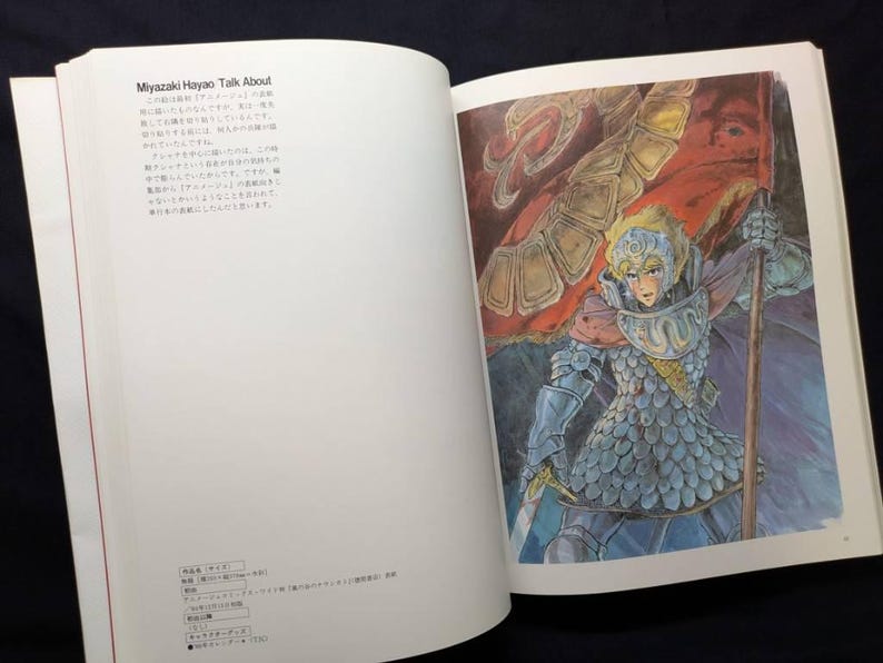 Pu&ograve; includere: Libro aperto con un'illustrazione colorata di un guerriero che tiene una bandiera. Il guerriero indossa un'armatura e un elmo. Il testo sulla pagina di sinistra recita "Miyazaki Hayao Talk About".