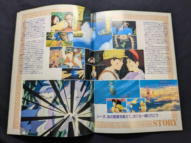 May include: An open book featuring multiple colorful anime-style illustrations from the film Castle in the Sky. The pages contain Japanese text, various scenes of characters in flight and dialogue, and a large graphic panel with black radiating lines.