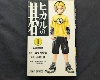 May include: A manga book titled "Hikaru no Go" volume 1. The cover features a character in a yellow shirt with the number 5, black shorts, and sneakers. Japanese text is visible on the cover.