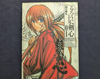 May include: A manga book titled "Rurouni Kenshin" with a cover illustration of a character with orange hair and a red robe. The book has Japanese text and the number "01" on the cover. The background is a dark blue.