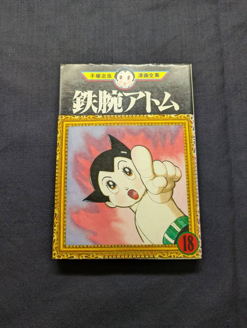 May include: Astro Boy manga volume 18. The cover features a colorful illustration of the character pointing with a surprised expression. The title is in Japanese with a gold frame and a red background.