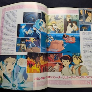 May include: A printed magazine spread featuring multiple colorful anime-style illustrations from the film Castle in the Sky. The pages contain Japanese text, character portraits, action scenes with flying vehicles, and a glowing blue pendant.