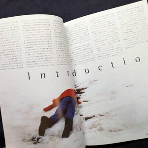 以下が含まれることがあります： ページに「Introduction」の文字が印刷された開いた雑誌。赤いジャケットと青いズボンを着た人が雪の中に横たわっています。その人は茶色のブーツを履いています。