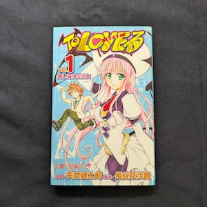 May include: A manga volume titled "To LOVEる" with a blue cover. The cover features a female anime character with pink hair and a male character. The text "Vol. 1" is visible, along with Japanese text and the "JUMP COMICS" logo.