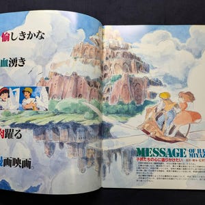 May include: A double-page spread illustration featuring a watercolor-style floating castle above clouds, with two small inset panels of characters and white birds. On the right, two figures ride a small flying machine, with Japanese text throughout.