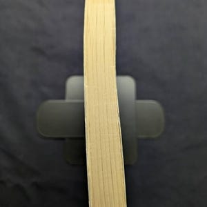 May include: A hardcover book with beige-colored pages, held upright by a black book stand. The book's spine is visible, showing the stacked pages. The background is a dark, solid color.