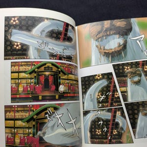 Pode incluir: Livro aberto com ilustra&ccedil;&otilde;es de mang&aacute;. Os pain&eacute;is retratam uma grande criatura azul clara com uma boca dentada e cenas de um edif&iacute;cio tradicional japon&ecirc;s com figuras em vestes vermelhas. O estilo art&iacute;stico &eacute; detalhado e colorido.