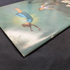 May include: A rectangular book cover featuring a teal background with an illustration of a person in a blue dress falling through the air, accompanied by another figure above, with Japanese text visible in the upper right corner of the cover.