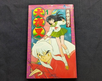 May include: A colorful manga book with the title "InuYasha" in Japanese. The cover features two anime characters, a girl in a school uniform and a boy in a red robe. The book is number 1 in the series.