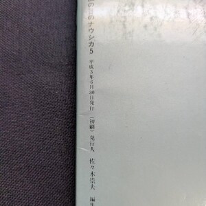 May include: A book with Japanese text. The cover is light blue with Japanese text in black. The text includes "ワイド版 風の谷のナウシカ5" and the date "平成3年6月30日". The book is on a dark gray surface.