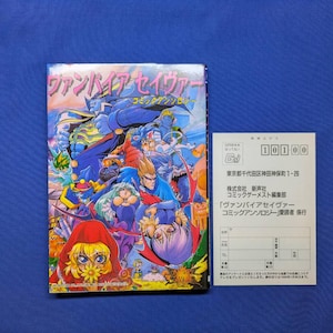May include: A Vampire Savior comic anthology book featuring a colorful manga-style cover illustration with various characters, accompanied by a white rectangular postcard with Japanese text and a postal code box printed in black ink.