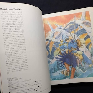 Pu&ograve; includere: Un libro aperto con testo e un'illustrazione colorata. L'illustrazione raffigura una figura in armatura blu con un'arma, in sella a una grande creatura azzurra. Lo sfondo presenta un cielo arancione e blu.