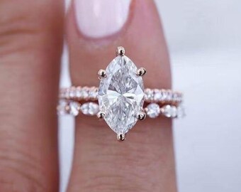 May include: A rose gold engagement ring set with a marquise-cut diamond. The main ring is paired with a band of smaller diamonds. The design is classic and elegant, suitable for a special occasion. The ring is a symbol of commitment.