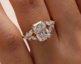 May include: A gold ring with a large, rectangular-cut diamond at its centre, complemented by smaller, marquise-cut diamonds. The ring's band is also embellished with smaller diamonds, creating a sparkling, elegant design.