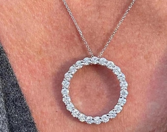 May include: A silver necklace with a circular pendant set with numerous sparkling gemstones. The pendant hangs from a delicate chain, creating a classic and elegant look. The necklace is shown against a neutral background.