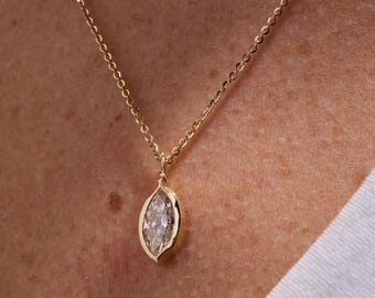 May include: A gold necklace featuring a marquise-cut diamond pendant. The pendant is set in a gold bezel and suspended from a fine gold chain. The necklace is displayed against a skin tone background.