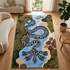 Puede incluir: Una alfombra rectangular que presenta una gran serpiente de patrón blanco y negro con múltiples cabezas serpenteando a través de un río azul claro. El paisaje incluye parches verdes texturizados, formas rocosas marrones y áreas de arena beige.