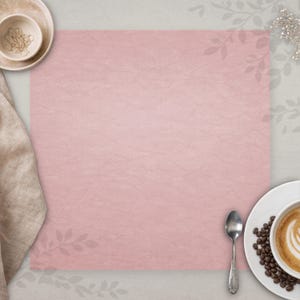 Pode incluir: Uma composição em plano com uma superfície rosa texturizada, um guardanapo de linho bege e uma tigela pequena com elementos decorativos. Um prato branco com uma xícara de café e grãos de café, e uma colher de prata também estão presentes. O fundo é cinza claro.