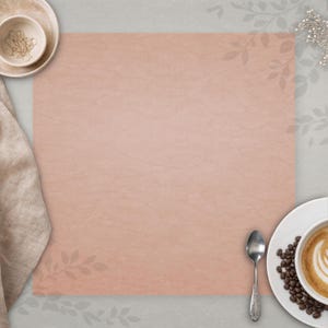 May include: A flat lay composition featuring a textured, blush-coloured paper surface. A white coffee cup with latte art and coffee beans sits on a plate. A small bowl with decorative items, a spoon, and a linen napkin are also present.