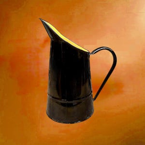 May include: A black enamel jug with a curved handle and a spout. The interior of the spout is yellow. The jug is set against an orange background. The jug is likely vintage or antique.
