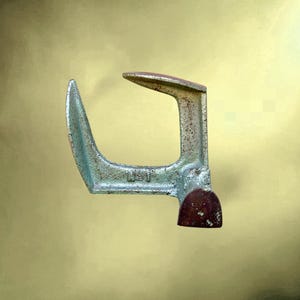 Op de afbeelding: Een gietijzeren schoenmakersaambeeld met een verweerde, metallic zilveren afwerking en zichtbare roestvlekken. Het gereedschap heeft een gebogen staander en een horizontale arm, met het cijfer 1 in reliëf op de zijkant van de basis.