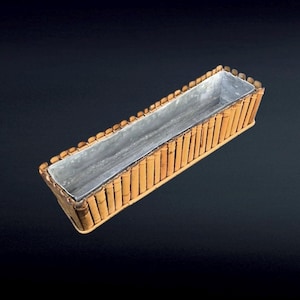 Puede incluir: Jardinera rectangular de bambú con interior de metal galvanizado. La jardinera está construida con postes de bambú verticales y un borde decorativo. El diseño es natural y rústico, adecuado para uso en interiores o exteriores.