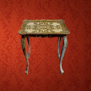 Puede incluir: Una mesa auxiliar cuadrada con un acabado envejecido en color crema y dorado. El tablero presenta un intrincado patrón de volutas en relieve con bordes festoneados. La mesa se apoya sobre cuatro patas delgadas y curvas que se estrechan hacia el suelo.