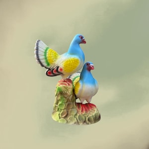 May include: A ceramic figurine of two colorful doves perched on a textured base. The doves have blue heads, yellow and white bodies, and red beaks. The base is green, brown, and red.