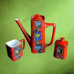 Puede incluir: Un juego de café de cerámica roja que incluye una tetera, un azucarero y una taza. El juego tiene un diseño único con formas geométricas en azul, amarillo y negro. La tetera tiene un pico largo y un asa, mientras que la taza y el azucarero son cuadrados.