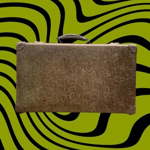 May include: A vintage brown suitcase with a textured surface and a handle. The corners are reinforced with metal. The background is a wavy pattern of black and green.