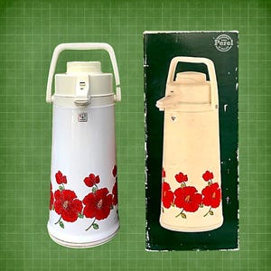 Puede incluir: Termo aislado blanco y crema con un diseño floral rojo. El termo tiene un asa y una boquilla. La caja de la derecha tiene el mismo diseño y la palabra "Perel".