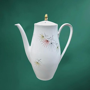 May include: White ceramic coffee pot with a lid and a gold handle. The pot features a long spout and a curved handle. It is decorated with colorful, stylized floral designs in red, yellow, and gray.
