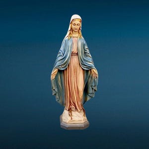 Puede incluir: Estatua de una mujer con velo blanco y capa azul, de pie sobre un pedestal. La estatua tiene una expresión serena y las manos extendidas. La mujer lleva un vestido rosa. El fondo es azul oscuro liso.