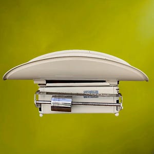 May include: A vintage cream-coloured scale with a curved top and a chrome-coloured weight. The scale has a rectangular base and a dial with measurement markings. The background is a solid, bright green.