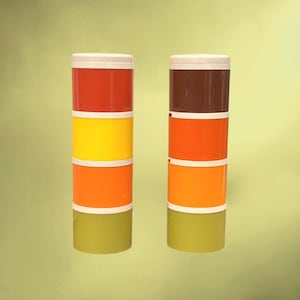 Peut inclure: Deux piles de contenants cylindriques colorés. Chaque pile est composée de quatre sections aux tons de rouge, jaune, orange et vert, surmontées d'un couvercle blanc. Les contenants sont probablement destinés au stockage ou à l'organisation.