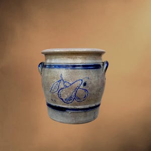 Peut inclure: Un pot en grès cylindrique avec une finition beige mouchetée et deux anses latérales. Il présente deux bandes horizontales bleu cobalt et un dessin au trait bleu représentant deux poires avec des feuilles sur le devant, ainsi que les initiales N.D.
