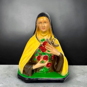 Puede incluir: Estatua religiosa de una mujer con velo negro y capa amarilla, sosteniendo una cruz y rosas. La estatua tiene una base verde y está pintada con colores marrón, amarillo y rojo.