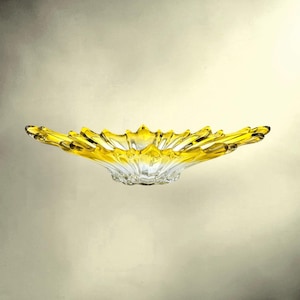 Puede incluir: Un cuenco de cristal poco profundo con un borde amarillo vibrante que se transforma en una base transparente e incolora. El cuenco tiene un borde festoneado en forma de pétalo con crestas radiantes que se extienden desde el centro hacia el borde ancho.