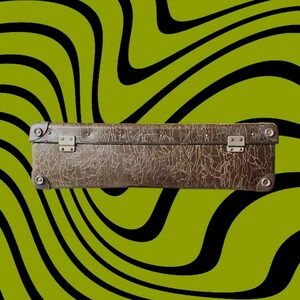 May include: A vintage brown suitcase with a textured surface and metal hardware. The suitcase is rectangular and has metal clasps and corner protectors. The background features a green and black wavy pattern.