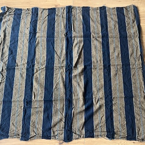 Pode incluir: Um tecido retangular com um padrão repetitivo de riscas verticais em azul-marinho escuro e castanho suave. O design inclui riscas brancas finas e nítidas que percorrem o centro de cada faixa castanha, criando uma estética linear e equilibrada.