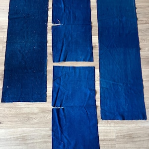 Könnte beinhalten: Vier rechteckige Stücke aus tiefblauem Indigostoff sind auf einer Fläche angeordnet. Zwei Stücke sind lang und schmal, während die anderen beiden kürzer und breiter sind, alle mit rohen, unversäuberten Kanten und einer gleichmäßigen, satten blauen Farbe.