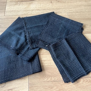 May include: Several rectangular pieces of dark navy blue fabric featuring a repeating pattern of small, light-coloured dots arranged in a grid. The fabric edges appear raw and unfinished, showing the texture of the woven material clearly.