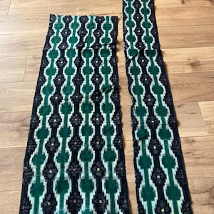 Op de afbeelding: Twee rechthoekige stukken stof met een donkerzwarte achtergrond en een herhalend geometrisch patroon in tinten bosgroen en lichtblauwgroen. Het ontwerp bestaat uit onderling verbonden cirkelvormen met kleine gele en rode accenten.