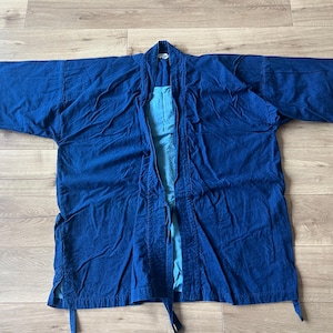 Puede incluir: Una chaqueta de color azul intenso abierta por delante con mangas anchas y un forro interior de color azul claro en contraste. La prenda presenta un cuello doblado, un cierre de lazo en la cintura y aberturas laterales en el dobladillo.