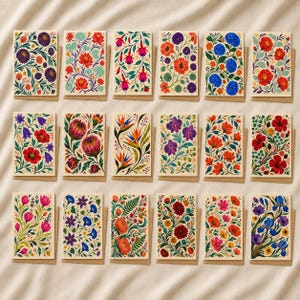 Könnte beinhalten: Eine Sammlung von achtzehn rechteckigen Grußkarten, angeordnet in drei Reihen, jede mit einer einzigartigen, farbenfrohen botanischen Illustration verschiedener Blumen, Blätter und Ranken auf cremefarbenem Grund, inklusive passender Umschläge.