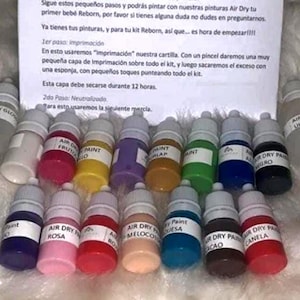 Può includere: Una collezione di piccoli flaconi di vernice in vari colori, etichettati con nomi come "Air Dry" e "Paint". I flaconi sono disposti con una nota scritta a mano sullo sfondo, che fornisce istruzioni per l'uso.