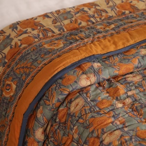 Può includere: Una trapunta trapuntata con un motivo floreale nei toni dell'arancione, blu e crema. La trapunta ha un bordo arancione e un bordo blu. Il design presenta un motivo floreale tradizionale.