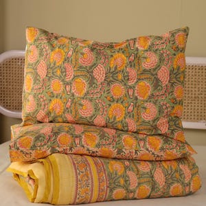 Puede incluir: Juego de cama con un diseño floral en amarillo, naranja y rosa sobre un fondo verde. El conjunto incluye una almohada y un edredón plegado. El edredón tiene un borde amarillo con rayas verticales.
